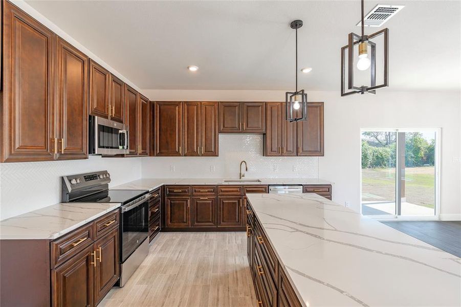 Kitchen with appliances with stainless steel finishes, light stone countertops, decorative light fixtures, light wood-type flooring, and sink