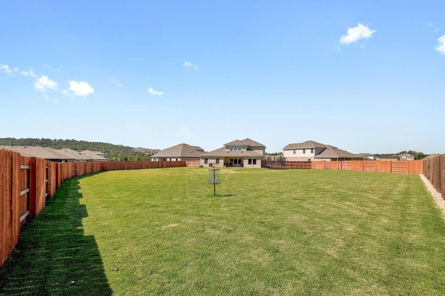 Expansive backyard featuring a large green lawn, full privacy fencing, and a two-story residence with a patio Expansive backyard featuring a large green lawn, full privacy fencing, and a two-story residence with a patio