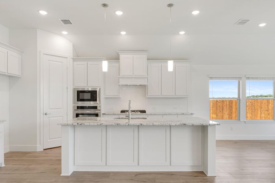 Kitchen with white cabinets, granite island, stainless steel appliances, and pendant lights over hardwood floors Kitchen with white cabinets, granite island, stainless steel appliances, and pendant lights over hardwood floors