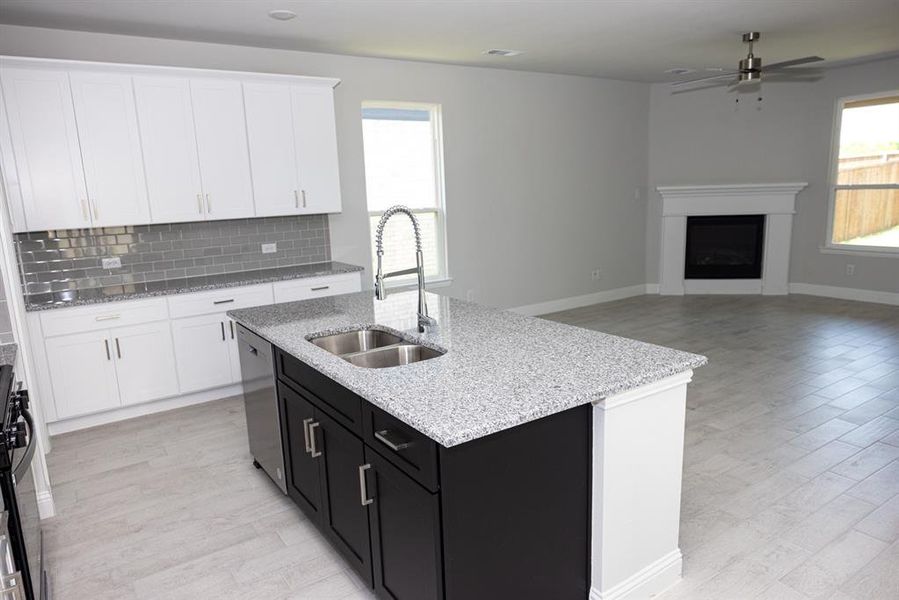 Kitchen featuring dishwasher, a fireplace, white cabinets, ceiling fan, and light wood-style flooring Kitchen featuring dishwasher, a fireplace, white cabinets, ceiling fan, and light wood-style flooring
