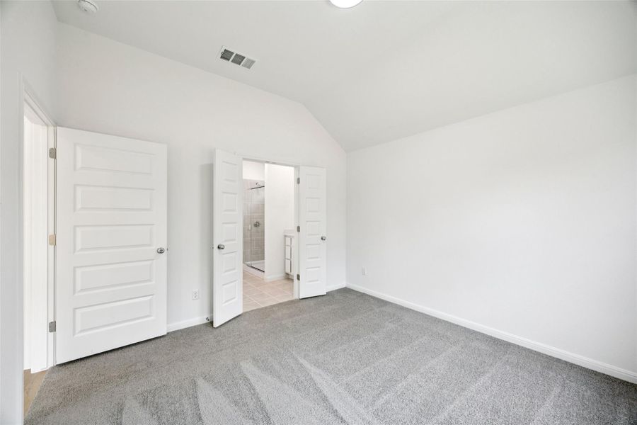 Unfurnished bedroom featuring vaulted ceiling, light carpet, and ensuite bathroom Unfurnished bedroom featuring vaulted ceiling, light carpet, and ensuite bathroom