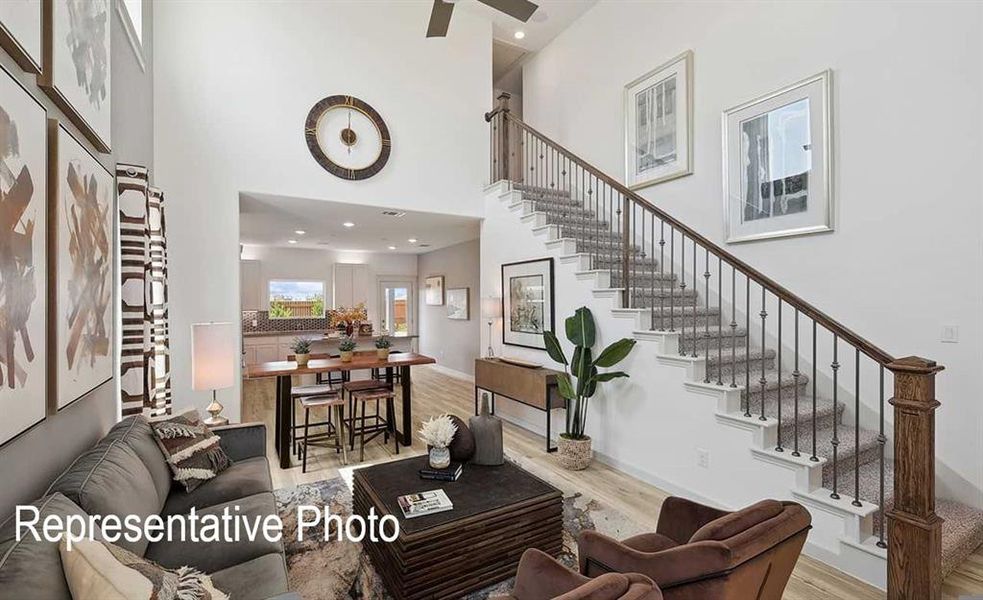 This open-concept living area features high ceilings, light-toned flooring, and a carpeted staircase with a dark wood handrail and iron balusters