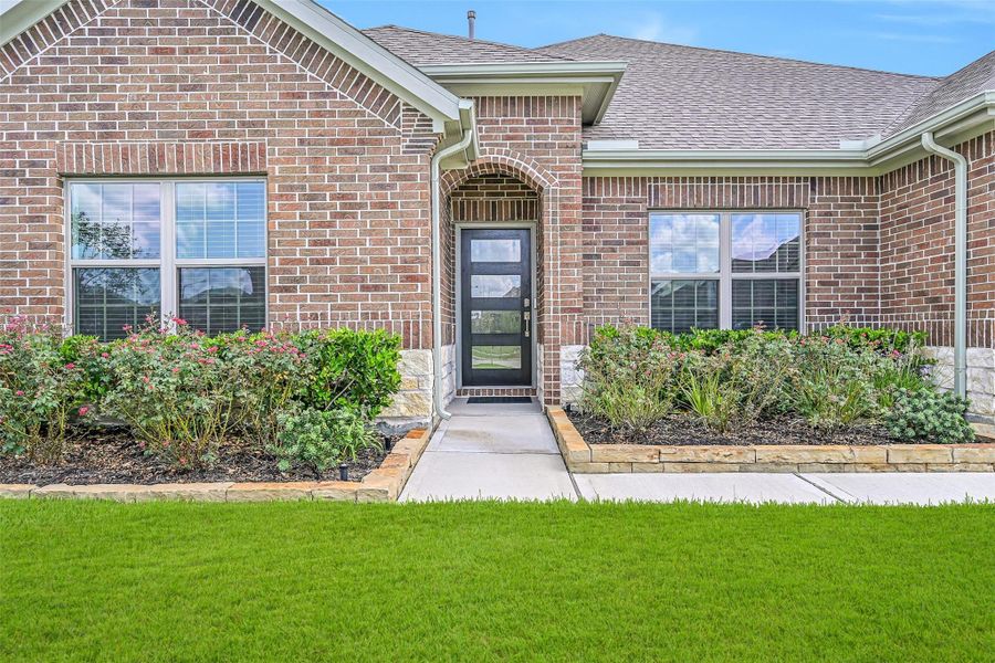 A closer look at the inviting front elevation showcases colorful established landscaping, brick & Austin limestone details and a recessed arched entry with a southwest facing contemporary style glass-panel front door. A closer look at the inviting front elevation showcases colorful established landscaping, brick & Austin limestone details and a recessed arched entry with a southwest facing contemporary style glass-panel front door.