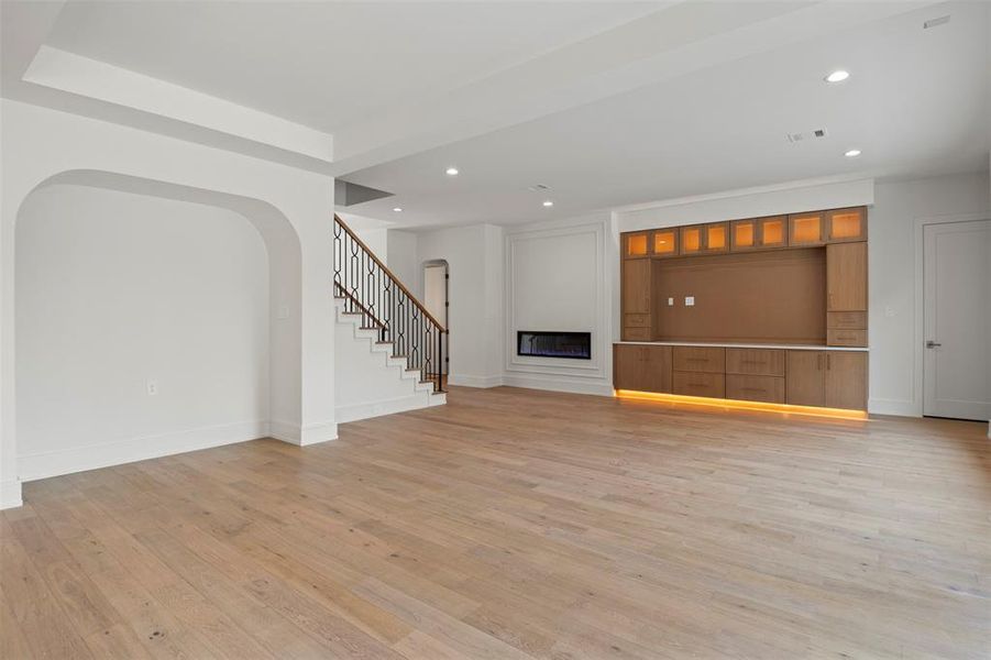 Unfurnished living room featuring light wood finished floors, arched walkways, a fireplace, recessed lighting, and stairs Unfurnished living room featuring light wood finished floors, arched walkways, a fireplace, recessed lighting, and stairs