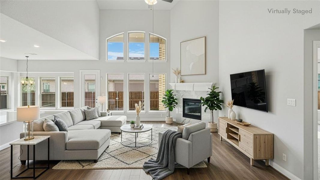 Living room featuring a high ceiling, a tiled fireplace, wood finished floors, a ceiling fan, and a chandelier Living room featuring a high ceiling, a tiled fireplace, wood finished floors, a ceiling fan, and a chandelier