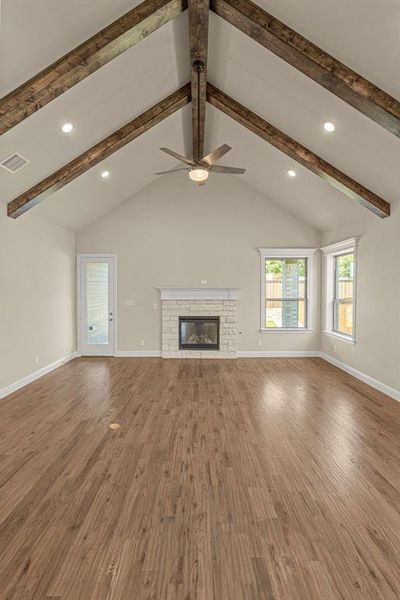 Unfurnished living room with vaulted ceiling with beams, hardwood / wood-style flooring, and a fireplace