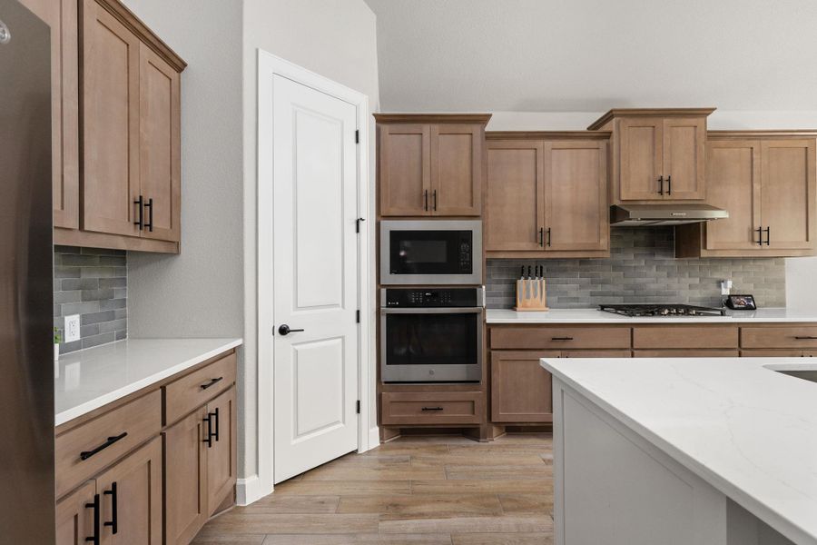 Two tone kitchen featuring backsplash, stainless steel appliances, light wood finished floors, light stone countertops, and two tone color scheme