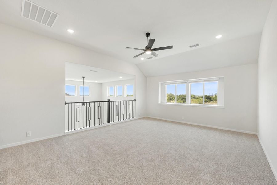 Open upstairs loft with carpet, ceiling fan, vaulted ceiling, and black metal railing overlooking lower level