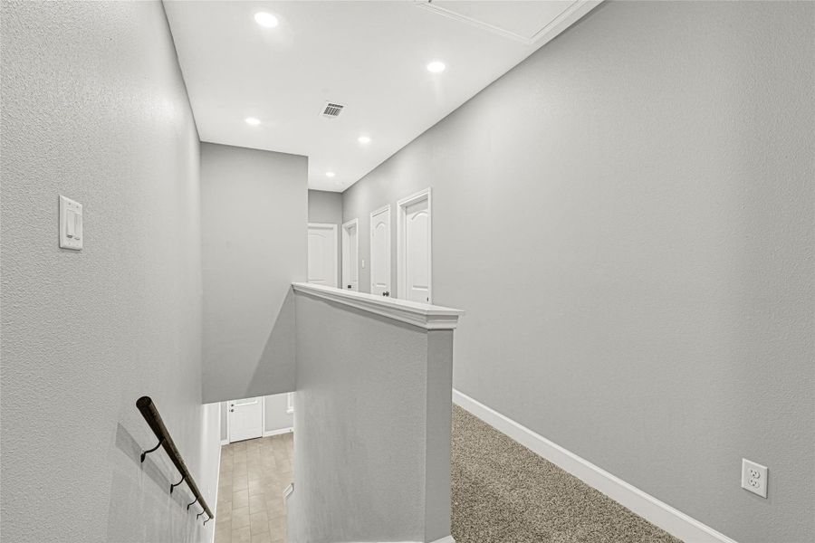 This photo shows a well-lit staircase and hallway with neutral gray walls and carpeted flooring. The space has recessed lighting and white trim, providing a clean and modern look.