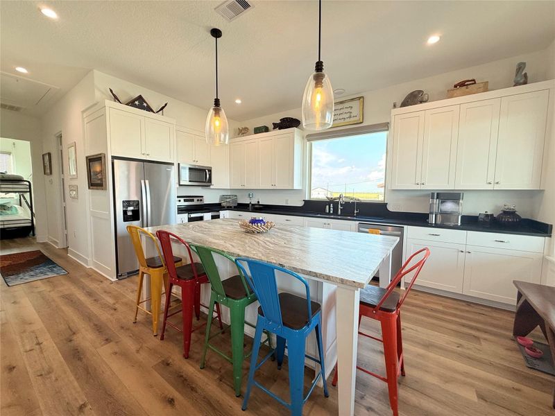 This open-concept kitchen and living area features modern appliances, a large island with seating, hardwood floors, and ample natural light. The space is accented by colorful chairs and nautical decor, creating a cozy and inviting atmosphere.