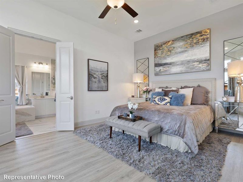 This room features light-colored flooring, a ceiling fan, and a view into a bathroom with a double vanity and a window