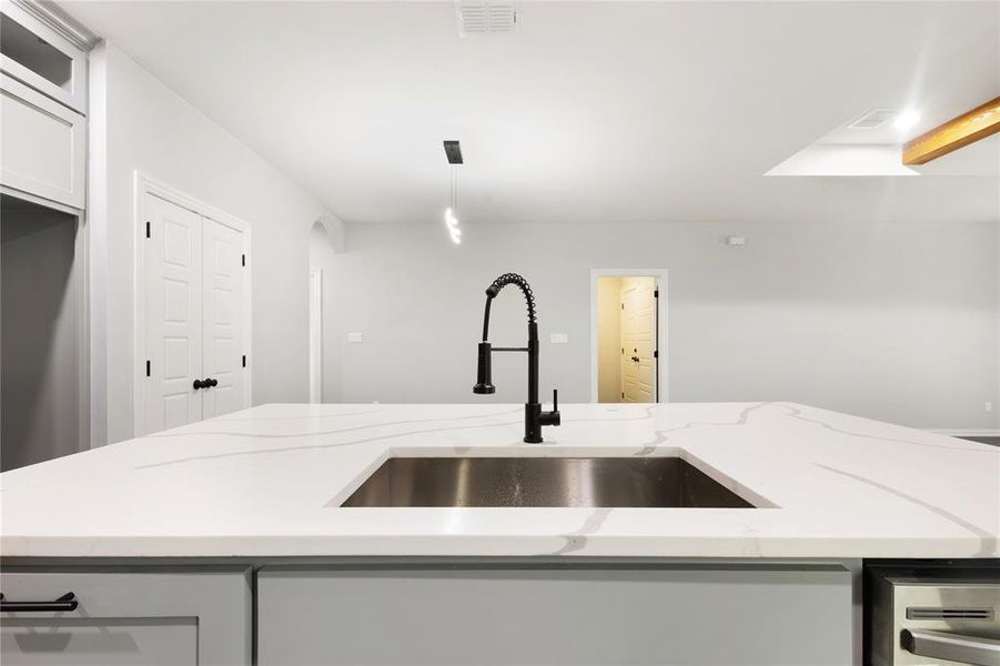Kitchen featuring light stone counters, hanging light fixtures, and white cabinetry