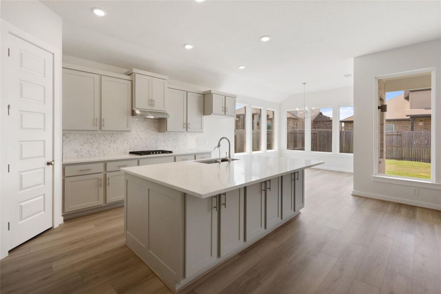 Kitchen featuring backsplash, a kitchen island with sink, light stone counters, recessed lighting, and decorative light fixtures