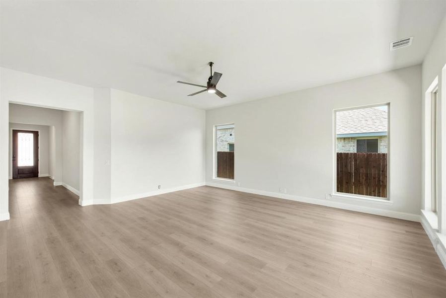 Spacious living area featuring light wood-finish flooring, white walls, and multiple windows Spacious living area featuring light wood-finish flooring, white walls, and multiple windows
