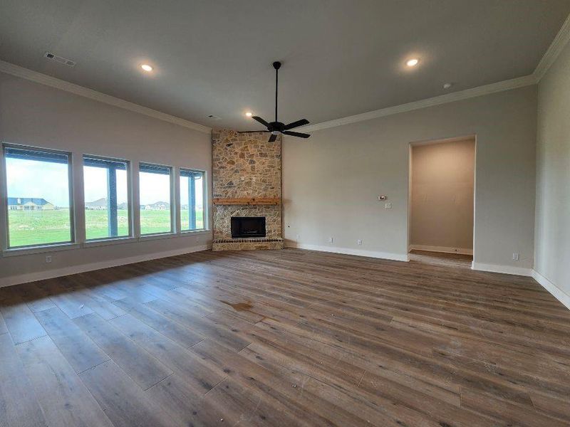 Spacious living area featuring a stone fireplace with a wood mantle, wood-finish flooring, a contemporary ceiling fan, and multiple windows