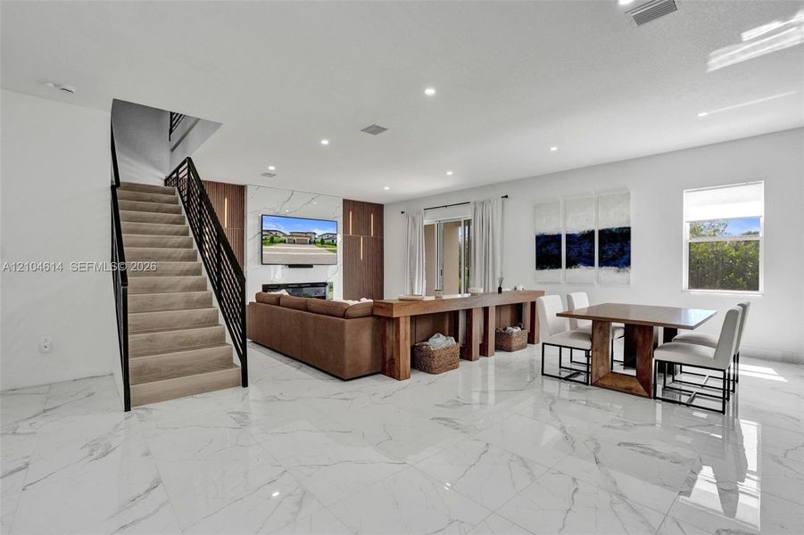 Spacious living area featuring polished tile flooring, recessed lighting, a modern fireplace, and a contemporary staircase with metal railings