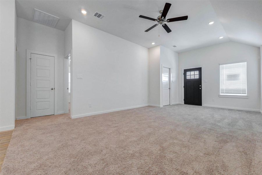 Bright living room with high ceilings, neutral walls, plush carpet, recessed lighting, ceiling fan, and a window near the front entry. This flexible space offers plenty of room for comfortable seating and connects easily to the rest of the home.