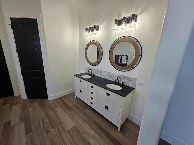 Bathroom with double vanity, dark wood finished floors, and decorative backsplash Bathroom with double vanity, dark wood finished floors, and decorative backsplash