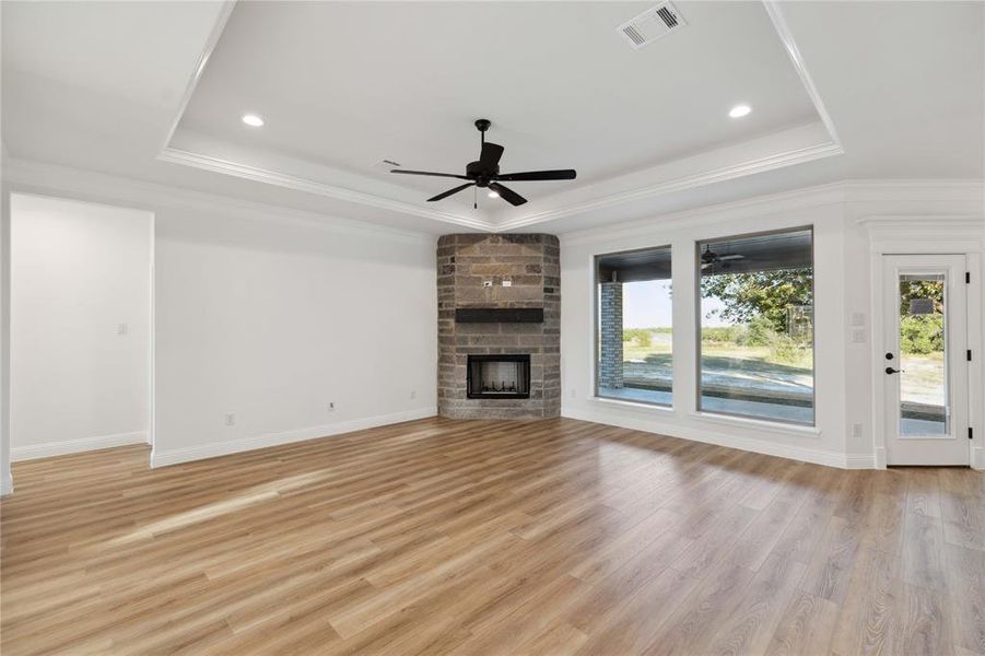 Unfurnished living room with a fireplace, a raised ceiling, light wood-type flooring, and ceiling fan