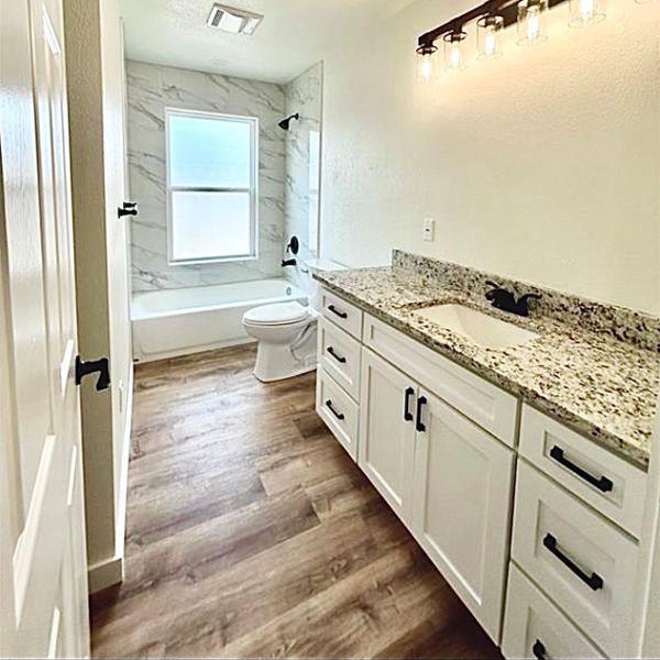 A sleek vanity with granite counters complements the tub and shower, featuring modern fixtures and durable flooring.