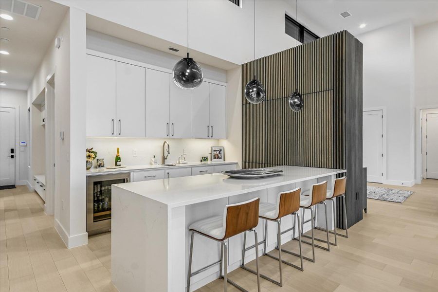 Kitchen with a breakfast bar area, white cabinets, wine cooler, pendant lighting, and light stone counters Kitchen with a breakfast bar area, white cabinets, wine cooler, pendant lighting, and light stone counters