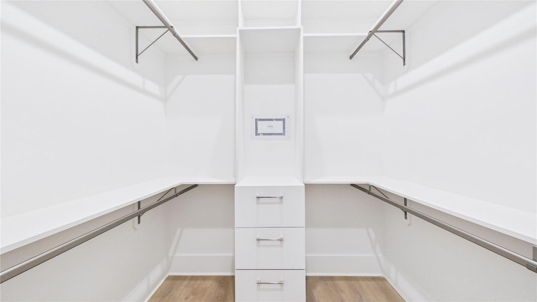 This image shows a spacious walk-in closet with white shelving, multiple hanging rods, and built-in drawers, offering ample storage space and modern design.