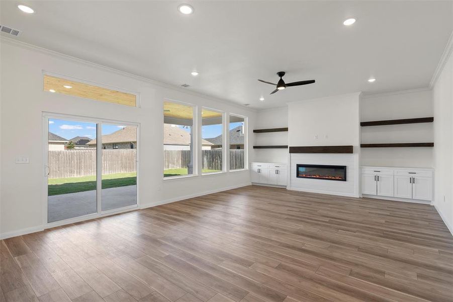 Unfurnished living room with recessed lighting, plenty of natural light, light wood-style floors, a glass covered fireplace, and crown molding