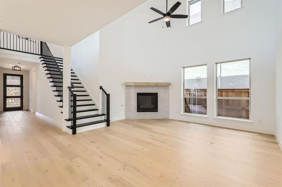 Unfurnished living room featuring a tiled fireplace, a high ceiling, light wood-type flooring, and ceiling fan