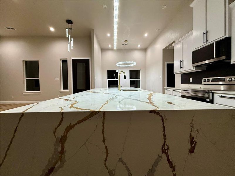 Kitchen featuring light stone countertops, stainless steel appliances, white cabinets, decorative light fixtures, and recessed lighting