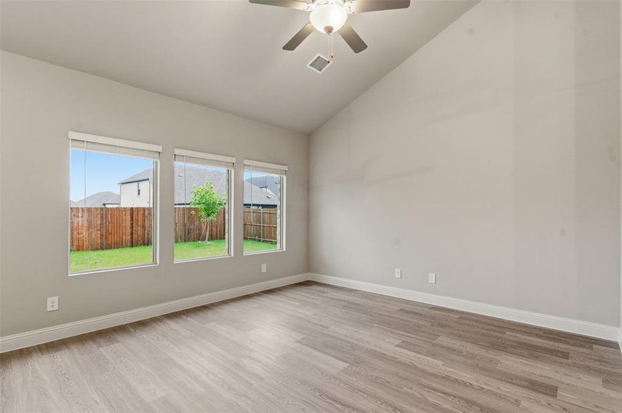 Living area with vaulted ceilings, a ceiling fan, and three windows offering views of the fenced yard