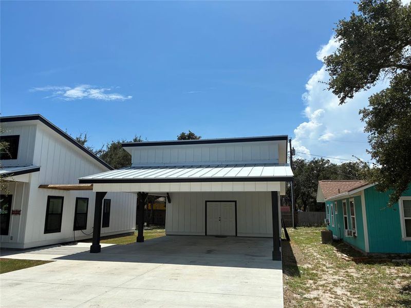 Modern inspired farmhouse with a standing seam roof, a metal roof, concrete driveway, a carport, and board and batten siding
