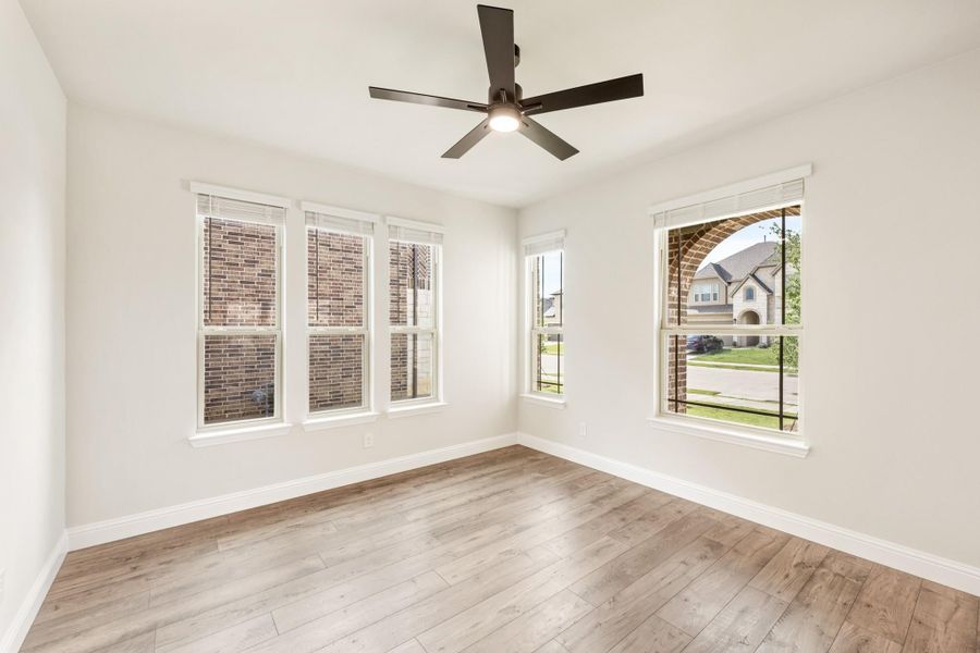 Empty room with hardwood floors, ceiling fan, and multiple windows with neighborhood views