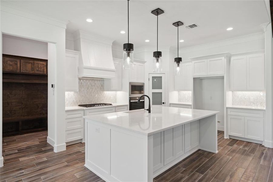 Kitchen with white cabinetry, custom exhaust hood, a center island with sink, and backsplash