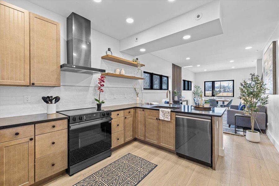 Kitchen with a peninsula, electric range, a sink, dishwasher, and wall chimney exhaust hood