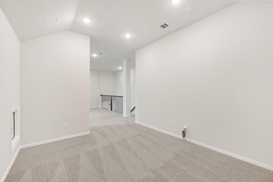 Empty upstairs loft with gray carpet, white walls, recessed lighting, and staircase railing visible in background Empty upstairs loft with gray carpet, white walls, recessed lighting, and staircase railing visible in background