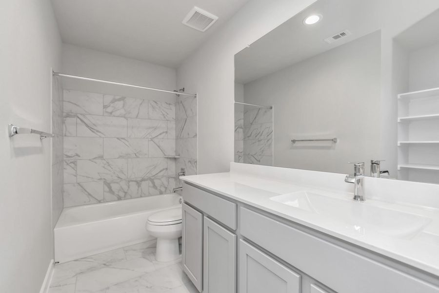 Secondary bath features tile flooring, bath/shower combo with tile surround, light stained wood cabinets, beautiful light countertop. Sample photo of completed home with similar floor plan. Actual colors and selections may vary.