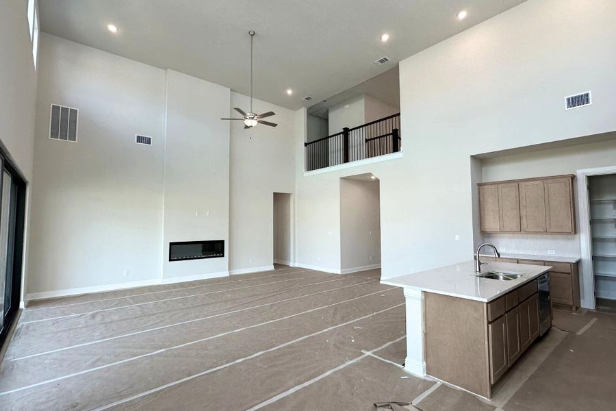Two-story living area featuring a linear fireplace, high ceilings with recessed lighting, and an open-concept kitchen island with a double sink and countertop