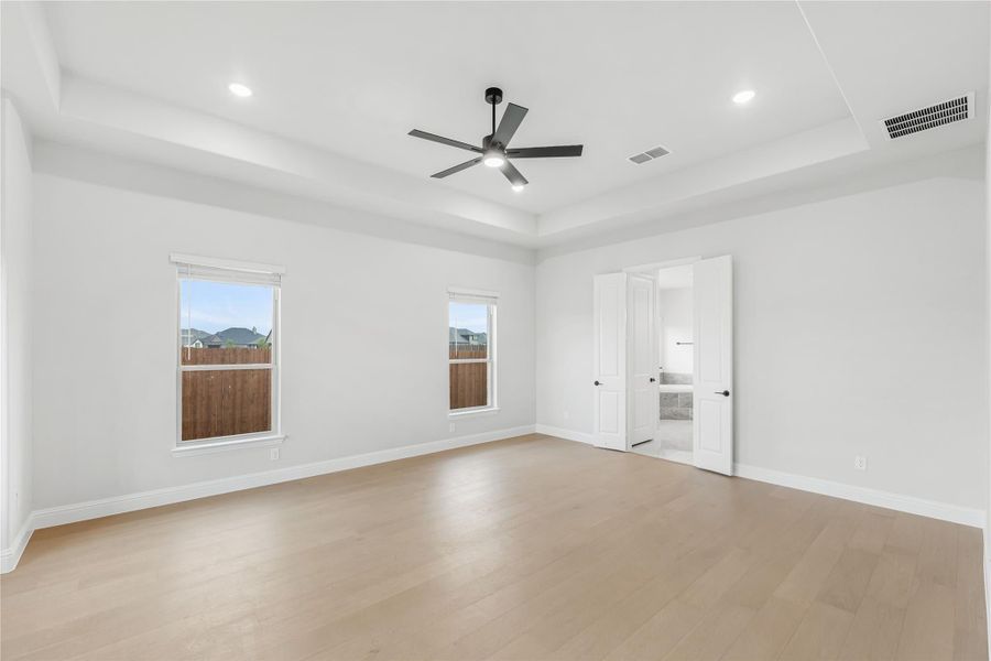 Empty bedroom with tray ceiling, ceiling fan, hardwood floors, and two windows