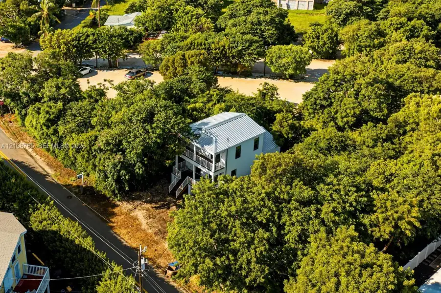 Two-story detached residence featuring a metal roof, stacked exterior balconies, and surrounding mature tree canopy Two-story detached residence featuring a metal roof, stacked exterior balconies, and surrounding mature tree canopy