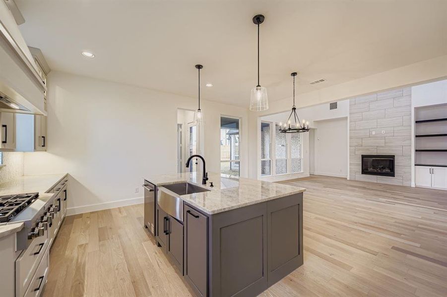 Kitchen with light wood finished floors, light stone counters, appliances with stainless steel finishes, hanging light fixtures, and recessed lighting