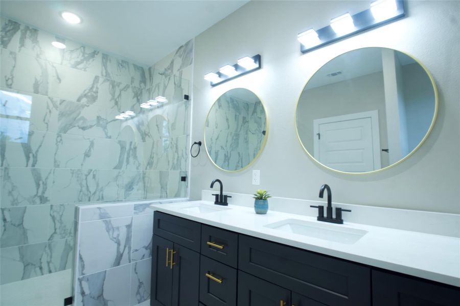 Full bath with double vanity and a marble finish shower