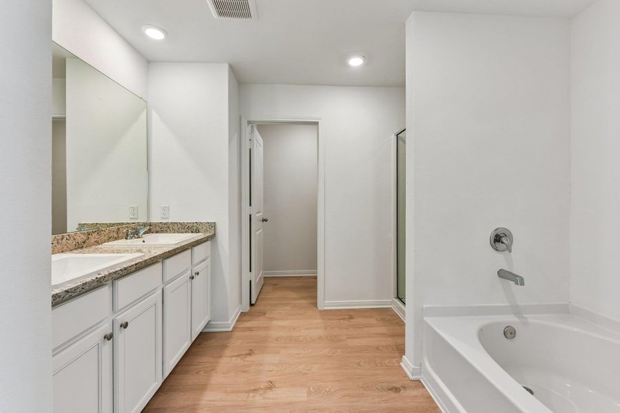 Bathroom featuring wood-finish flooring, a double vanity with stone-finish countertop and undermount sinks, a built-in bathtub with polished chrome fixtures, and a glass-enclosed shower