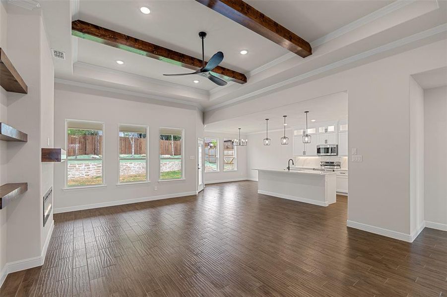 Unfurnished living room featuring beamed ceiling, ornamental molding, ceiling fan, and dark hardwood / wood-style floors