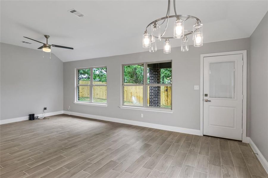 Unfurnished room with ceiling fan with notable chandelier, vaulted ceiling, and light wood-type flooring