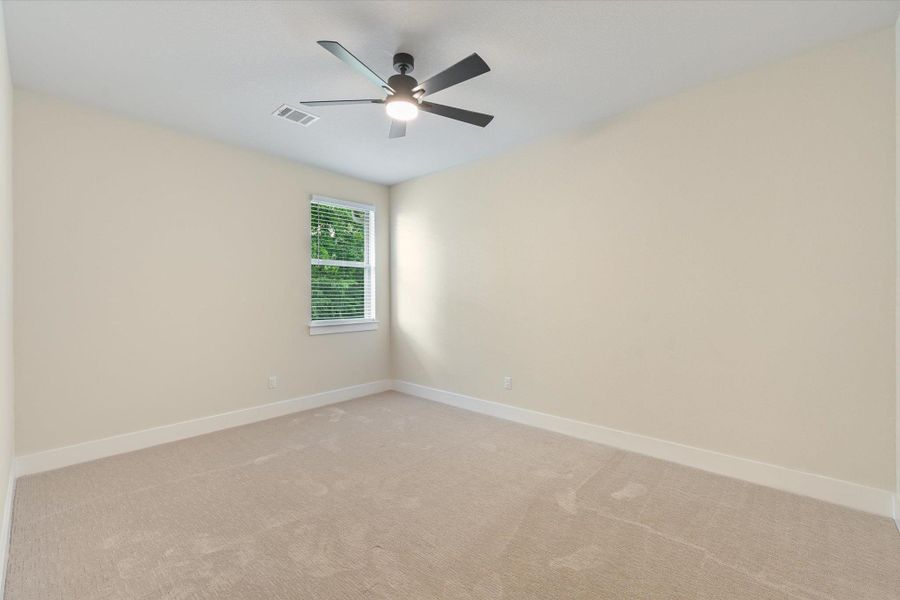 A well-lit bedroom with fresh carpeting and a modern ceiling fan, offering a comfortable personal retreat.