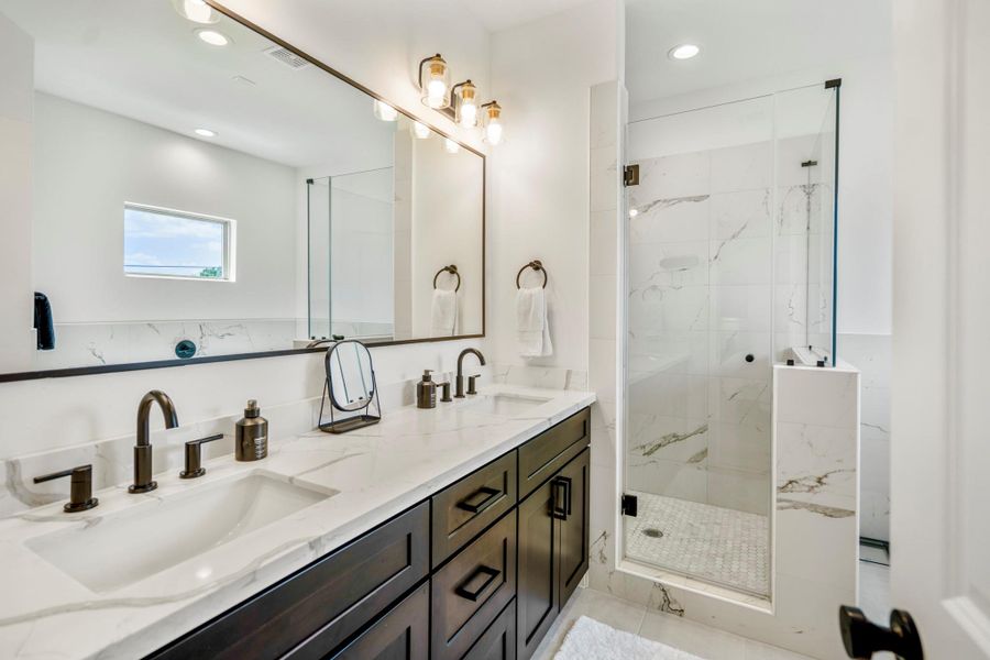 Spa-inspired bathroom complete with double sinks, full-width mirrors, modern accents, a glass shower, and a luxurious soaking tub.