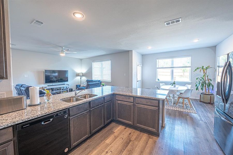 Kitchen featuring dark brown cabinets, black dishwasher, dark wood-type flooring, stainless steel fridge, and light stone countertops