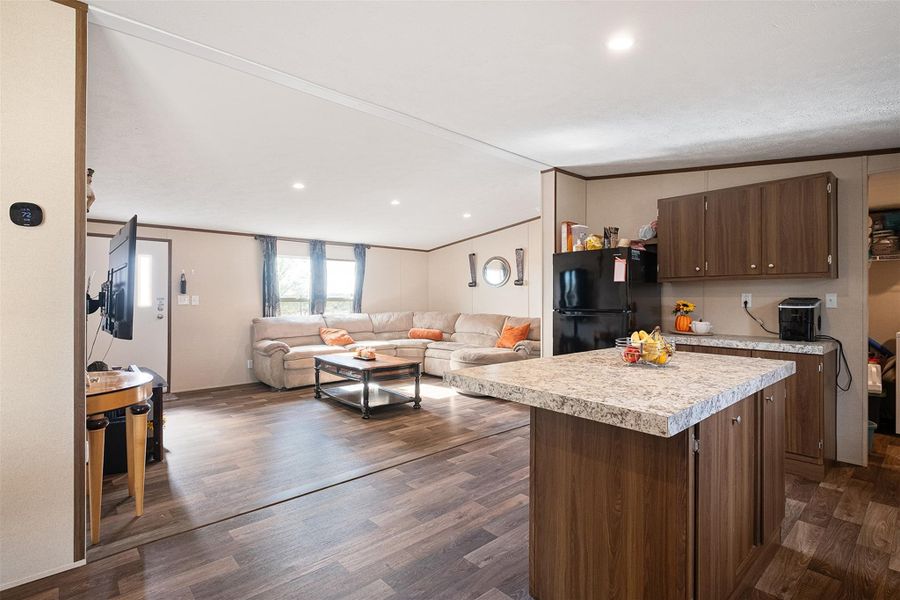 Kitchen featuring a kitchen island, light countertops, open floor plan, dark wood-type flooring, and freestanding refrigerator