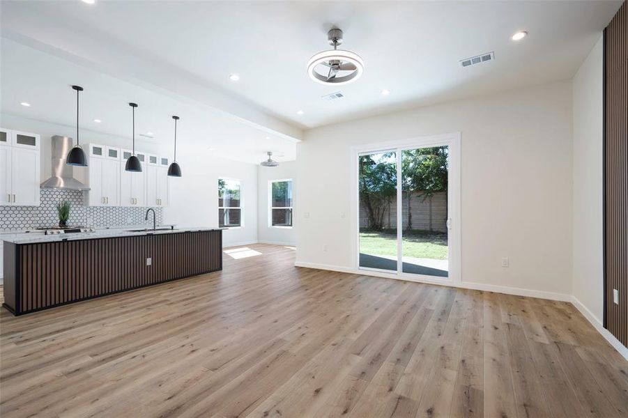 Kitchen with white cabinets, backsplash, hanging light fixtures, light wood-type flooring, and wall chimney exhaust hood