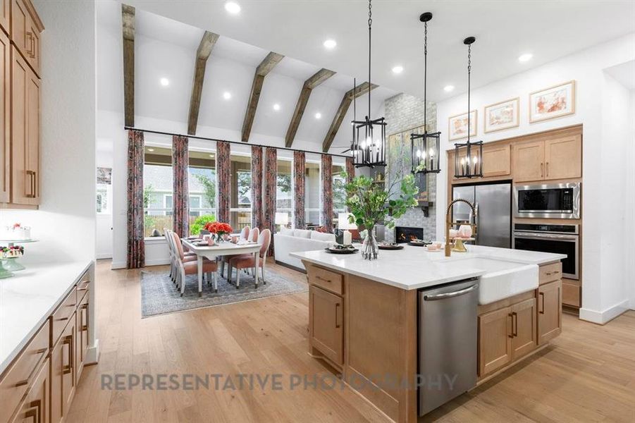 Kitchen featuring decorative light fixtures, stainless steel appliances, light brown cabinets, light wood-style flooring, and light stone countertops